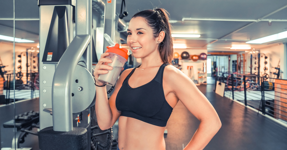 A woman drinking muscle-building supplements while at the gym.