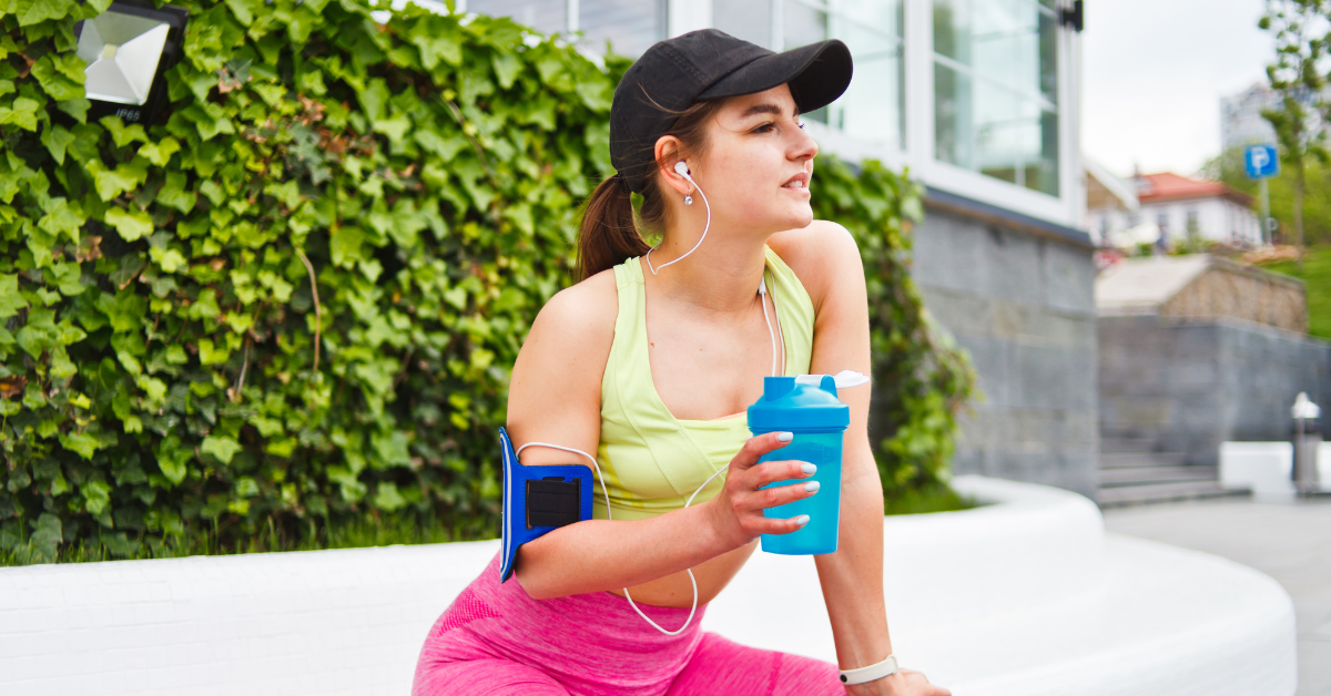 Image of a woman resting mid-workout with a shaker cup filled with supplements, related to the query "What supplements should I take when working out".